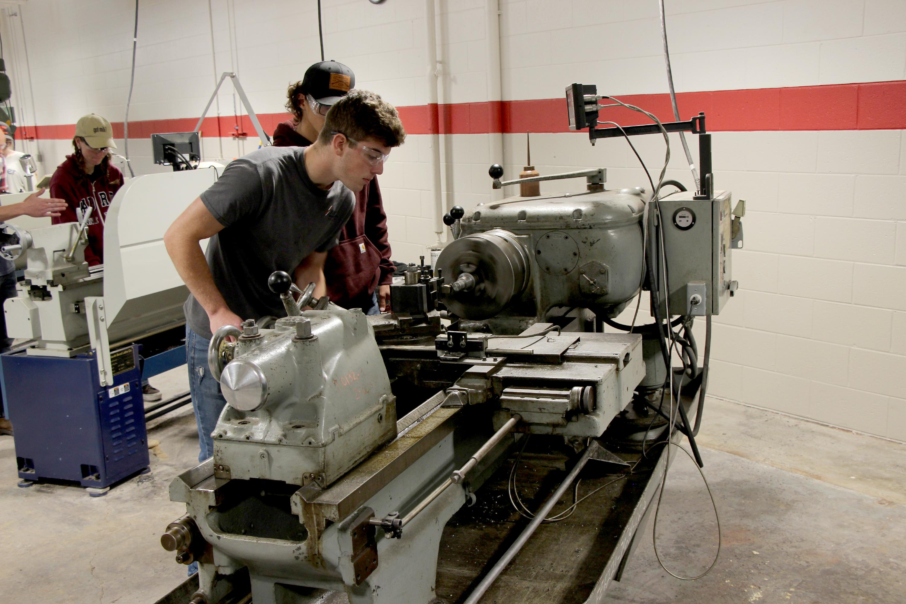 Two students work on a piece of equipment in the manufacturing lab